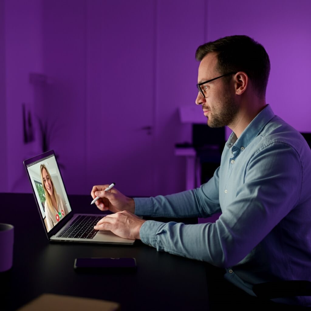 Man sitting in front of a MacBook, having a virtual meeting with a woman